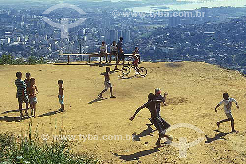  People playing soccer at the a favela mountain top with Rio de Janeiro city center view. 
