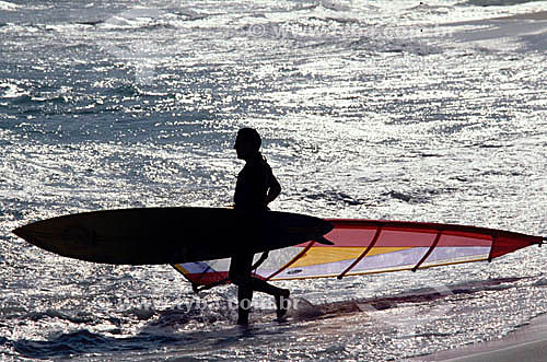  Silhouette of windsurfer holding his board and walking along the beach 
