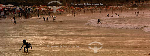 Beach scene: Silhouette of children playing on the sea in the foreground and the background full of umbrellas and people on the sand - Salvador city - Bahia state - Brazil 