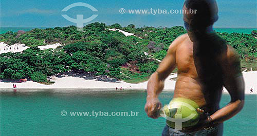  Man cutting coconut with the dunes of Lagoa de Abaeté (Abaete Lagoon) and the sea in the background - Salvador city - Bahia state - Brazil 