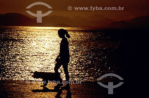  Silhouette of a woman and a dog walking in the sidewalk 