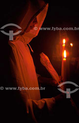  Person with hood praying with candles in the background 