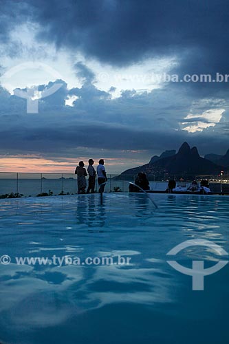  Silhouette of people enjoying the sunset on the top floor of Fasano Hotel at Ipanema Beach - swimming pool in the foreground and Morro Dois Irmaos (Dois Irmaos Mountain) in the background  - Rio de Janeiro city - Brazil
