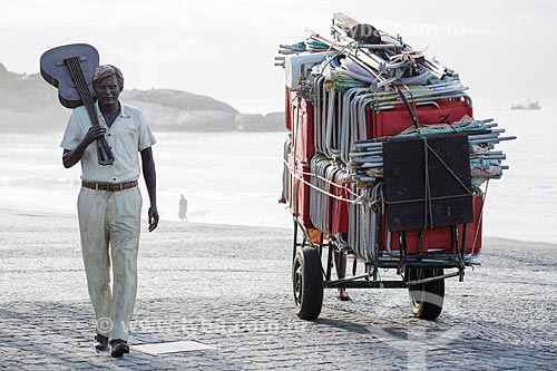  Man carrying a cart with beach chair near to statue of maestro Tom Jobim on Arpoador Beach boardwalk  - Rio de Janeiro city - Rio de Janeiro state (RJ) - Brazil