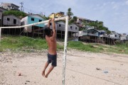 Child playing on a goalpost in a local soccer field with stilt houses in the background. - Tefe city - Amazonas state (AM) - Brazil